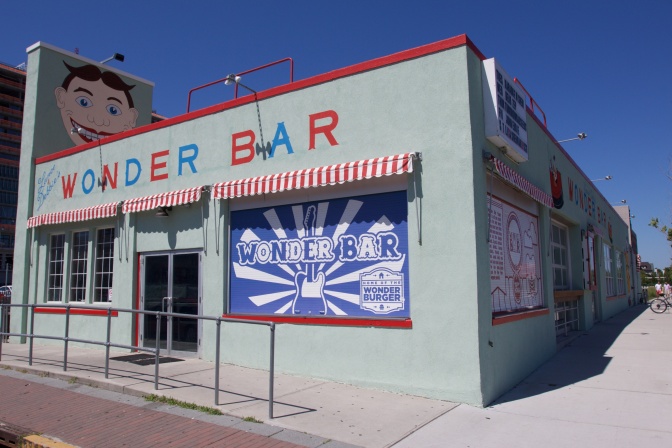 Exterior view of Wonder Bar, a bar and grill. The letters for Wonder Bar are alternating in red and blue on the marquis. A smiling face painting is on the chimney.