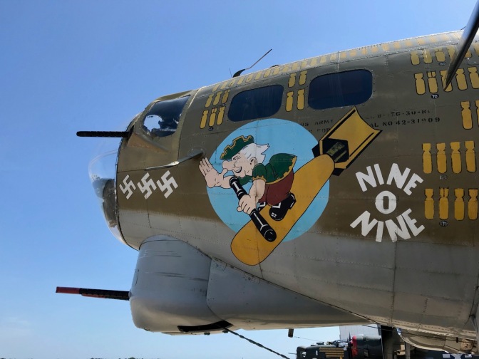 Cockpit of B-17 with emblem of George Washington on falling bomb with words NINE O NINE beside him.