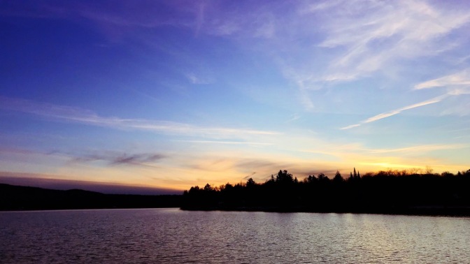 Sunset sky along tree-lined lake.