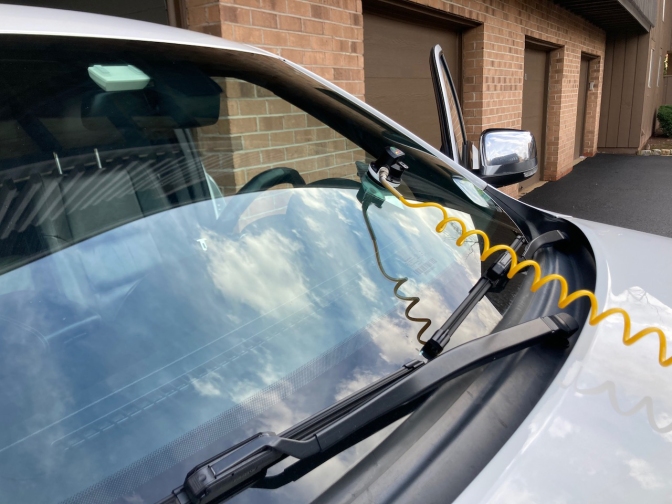 Device attached to windshield of Jeep Gran Cherokee. A yellow cable stretches from the device to the Safelite van.