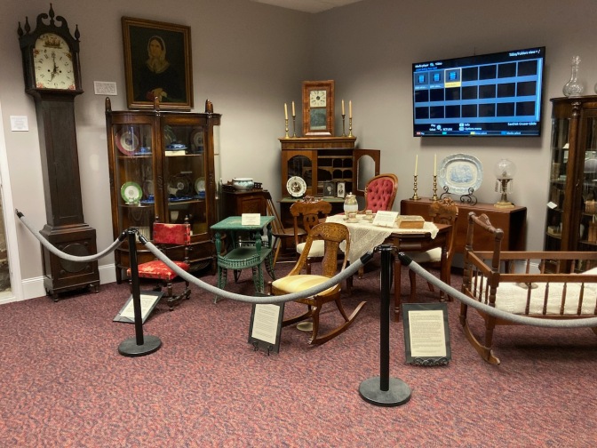 Exhibits in museum containing artifacts of Bolling family life, including a grandfather clock, a rocking chair, tables, dressers, cabinets, and a cradle.